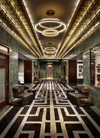 Una lussuosa hall d'hotel con un tappeto a motivi geometrici, lampadari moderni e sedute in pelle.