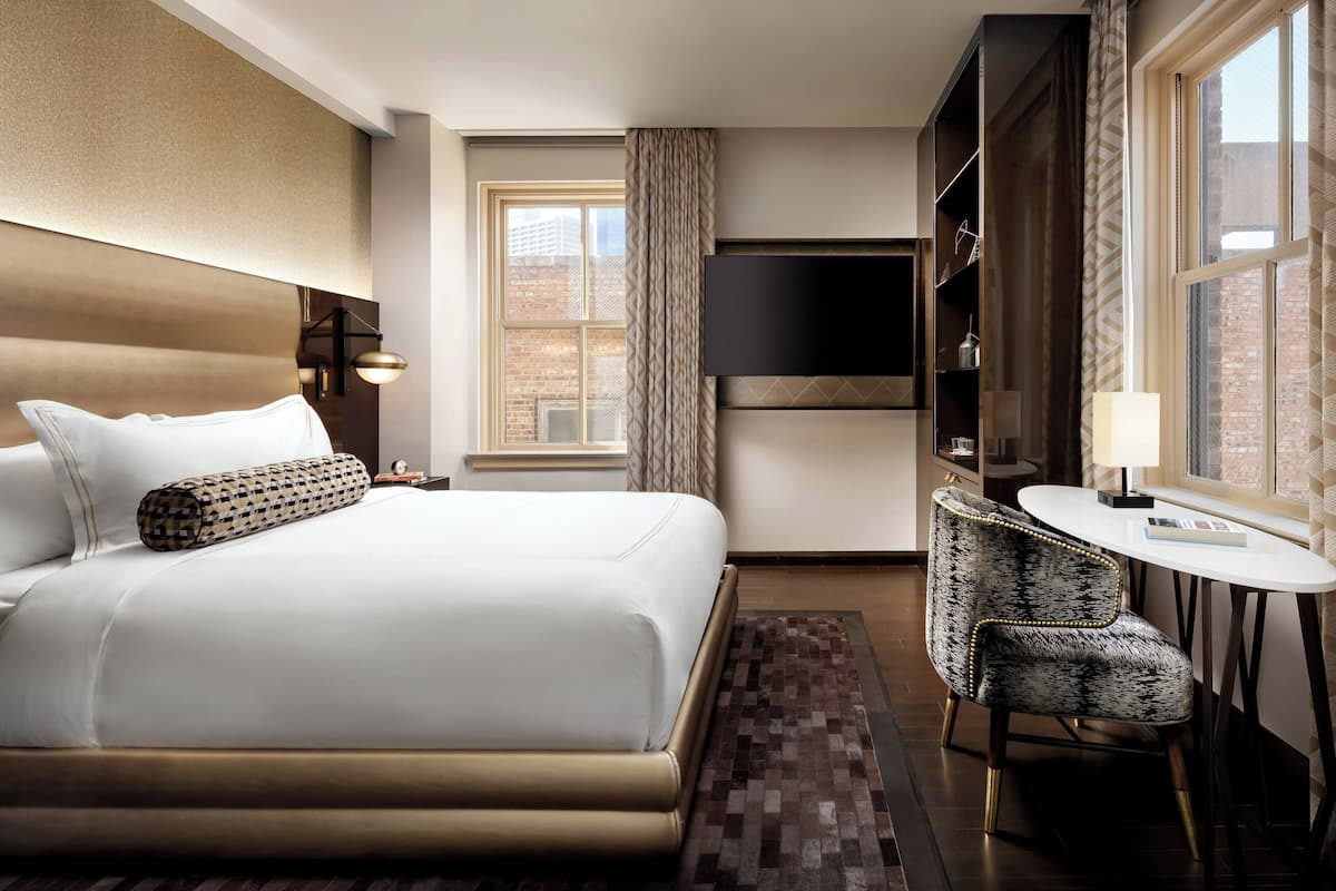 A hotel room with a large bed, a desk with a chair, a television, and a window with curtains.