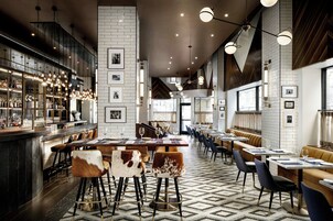 Un ristorante moderno con area bar, soffitti alti e una varietà di posti a sedere, tra cui sgabelli da bar e tavoli.