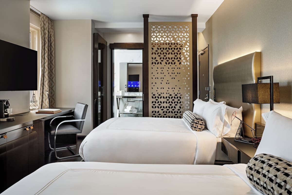 A hotel room with a bed, a desk, a chair, a TV, and a decorative partition.