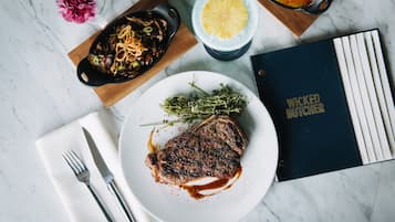 A steak with sauce, a book titled 'Wicked Witcher', and a dessert on a marble table.