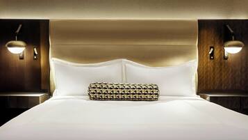 A hotel room with a large bed, a headboard, two bedside lamps, and a patterned throw pillow.