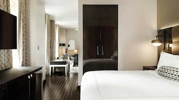 A hotel room with a large bed, a desk, a chair, a TV, and a wardrobe.