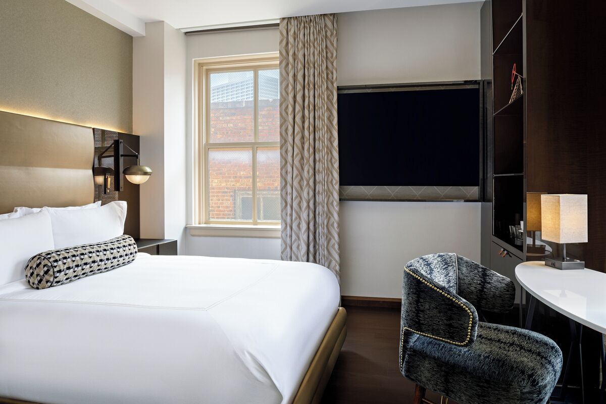 Ett hotellrum med en stor säng, ett skrivbord, en stol, ett fönster med gardiner och en platt-TV.