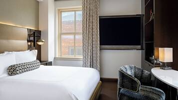 A hotel room with a large bed, a desk, a chair, a window with curtains, and a flat-screen TV.
