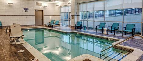 Una piscina interior con sillas de descanso, un vestuario y vistas al exterior.