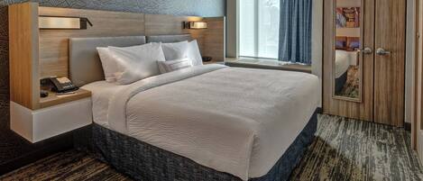 Una habitación de hotel moderna con una cama grande, una mesita de noche con teléfono, una lámpara de pared y un amplio ventanal con cortinas.