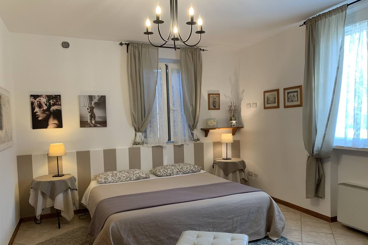A bedroom with a large bed, two bedside tables with lamps, a chandelier, and framed pictures on the walls.
