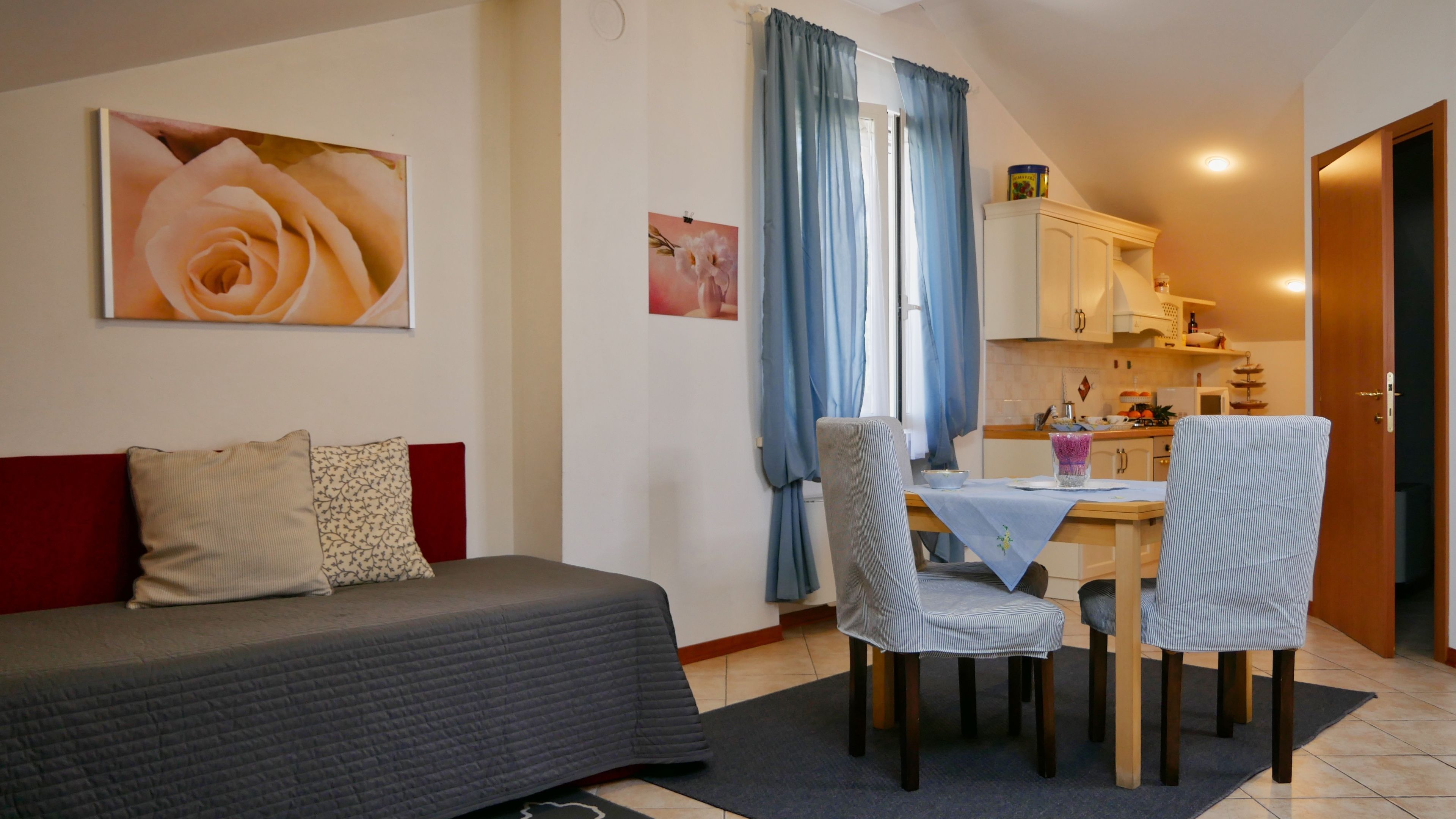 A compact living space with a sofa, a dining table with chairs, a kitchen area, and a door leading to another room.