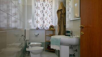 A bathroom with a toilet, bidet, sink, and a shower area.