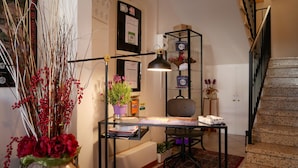 A hotel room with a desk, a chair, a potted plant, a lamp, and a staircase.