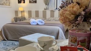 A hotel room with a neatly made bed, a breakfast tray with teacups and a floral arrangement, and a bedside table with a lamp.