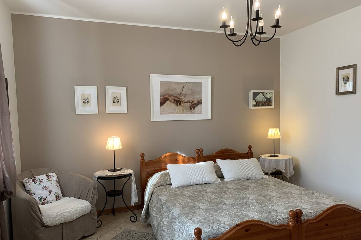 A bedroom with a wooden bed, two bedside tables with lamps, a chair, and framed pictures on the wall.