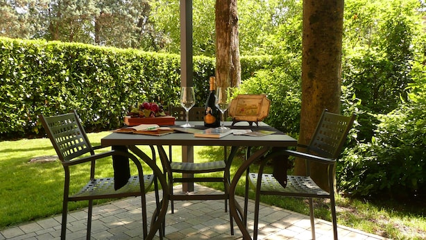 An outdoor patio with a table set for two, surrounded by greenery.