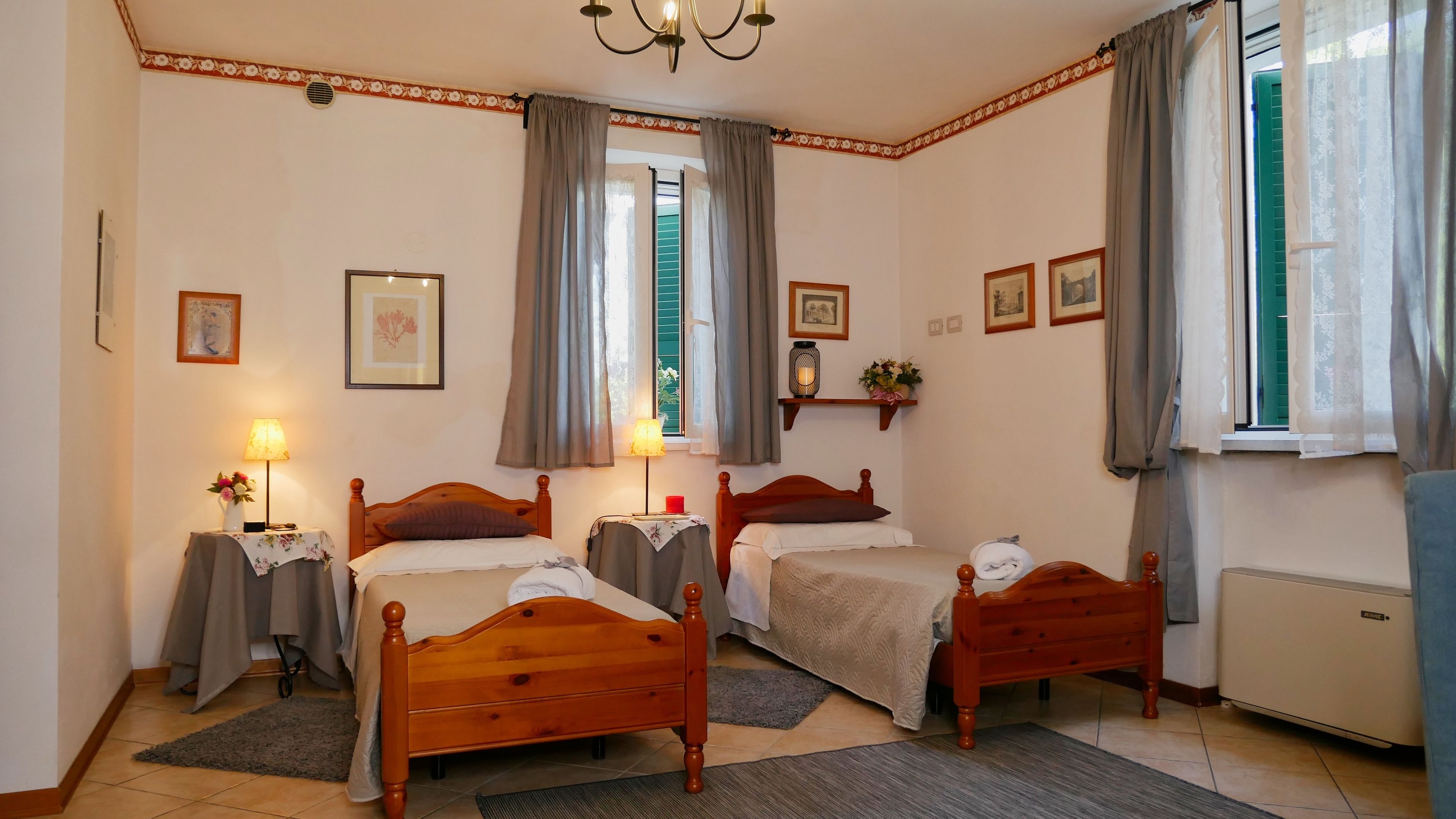 Une chambre d’hôtel avec deux lits en bois, un lustre, un radiateur et une fenêtre avec des rideaux.