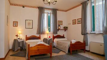 Une chambre d’hôtel avec deux lits en bois, un lustre, un radiateur et une fenêtre avec des rideaux.