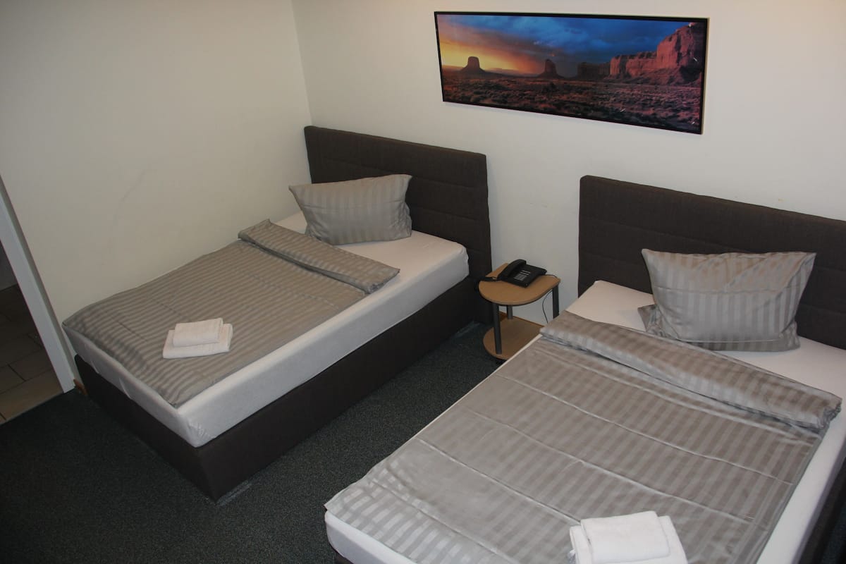 Habitación de hotel con dos camas individuales, una mesita de noche, un teléfono y un cuadro de un paisaje desértico.