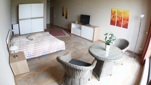 A bedroom with a bed, a TV, a desk, and two wicker chairs. - Sportpark Hotel (Bitburg)