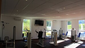 A gym with exercise equipment, large windows, and a flat-screen TV on the wall. - Sportpark Hotel (Bitburg)