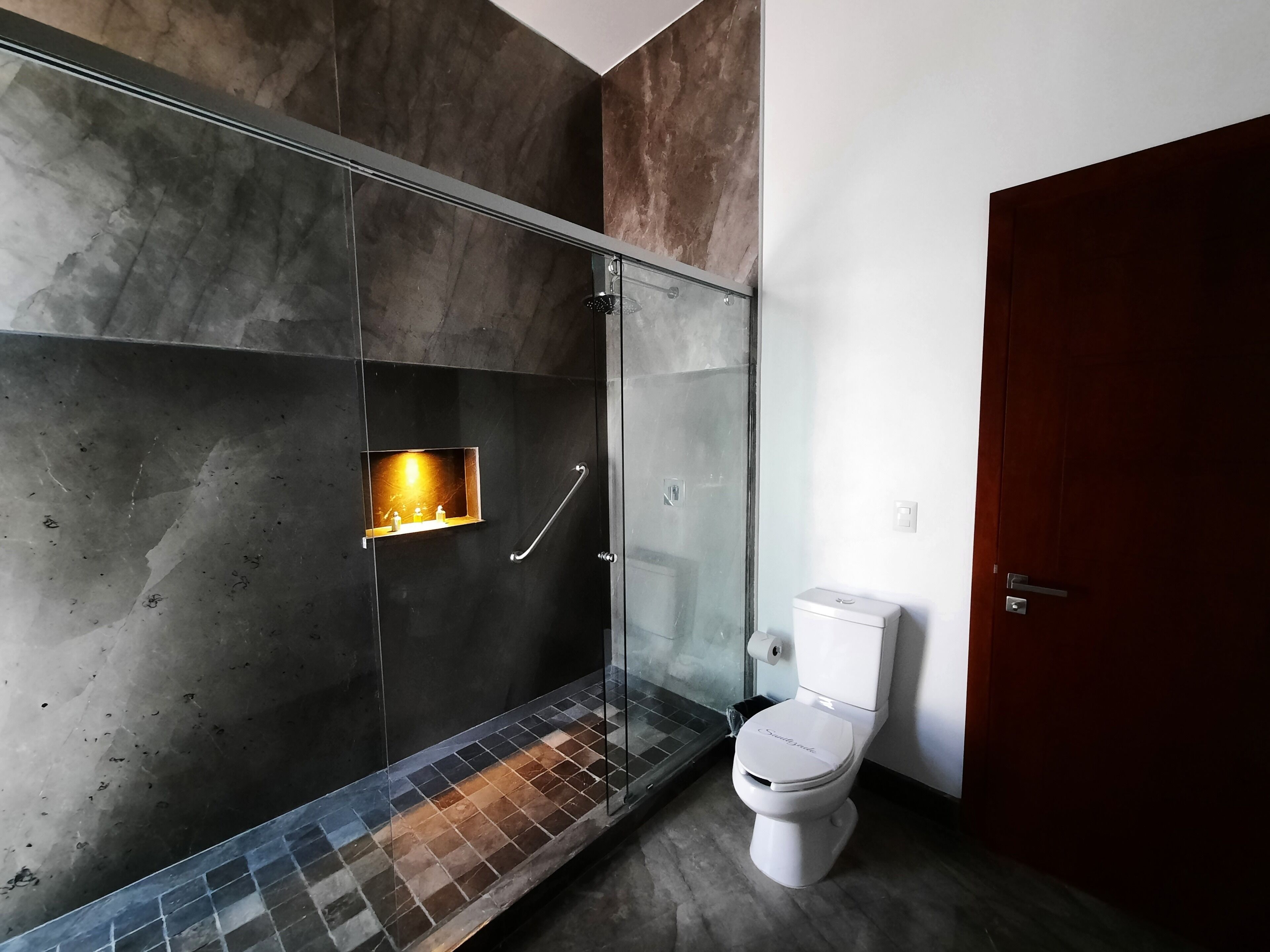 A modern bathroom with a glass-enclosed shower, a toilet, and a small shelf with toiletries.