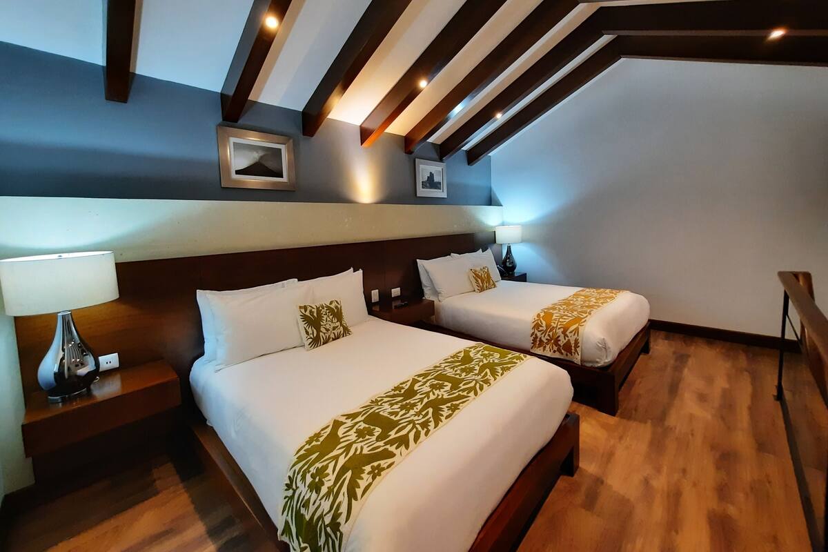 Une chambre d’hôtel avec deux lits, un plancher en bois et un plafond en pente avec des poutres apparentes.