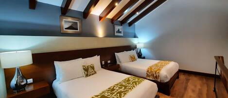 A hotel room with two beds, wooden floors, and a sloped ceiling with exposed beams.