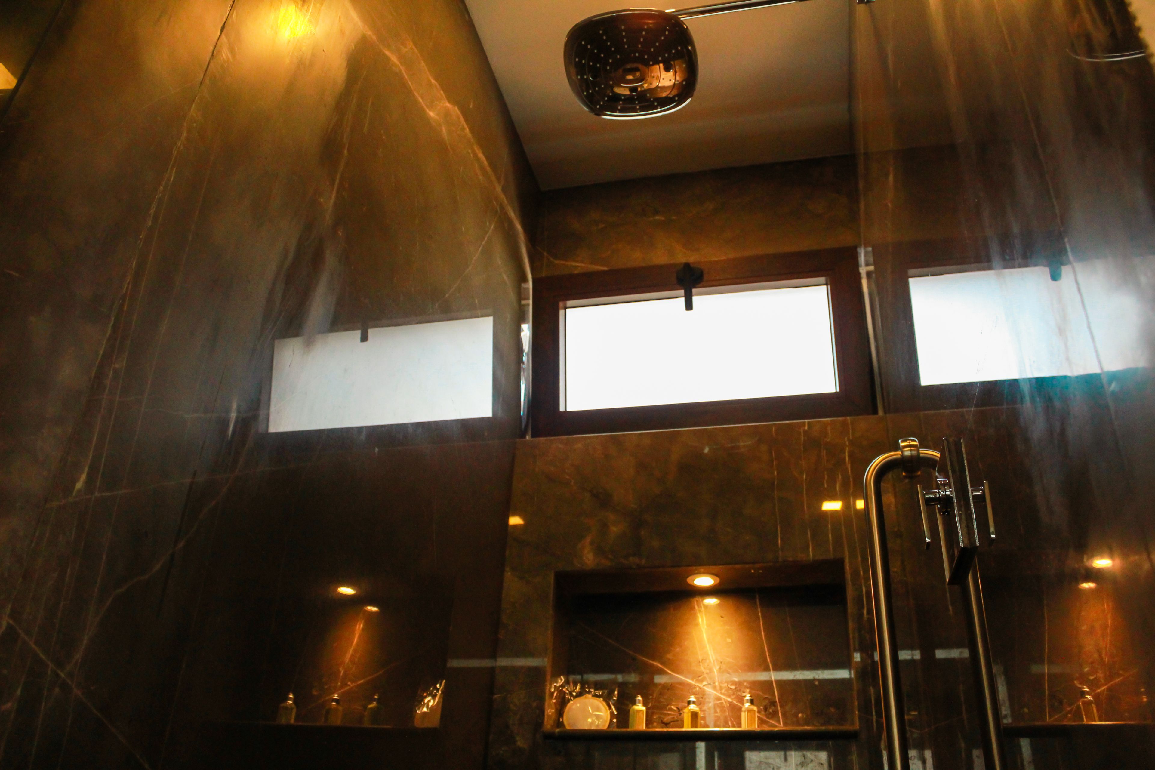 Een moderne badkamer met donkere marmeren wanden, een douche en een plank met toiletartikelen.
