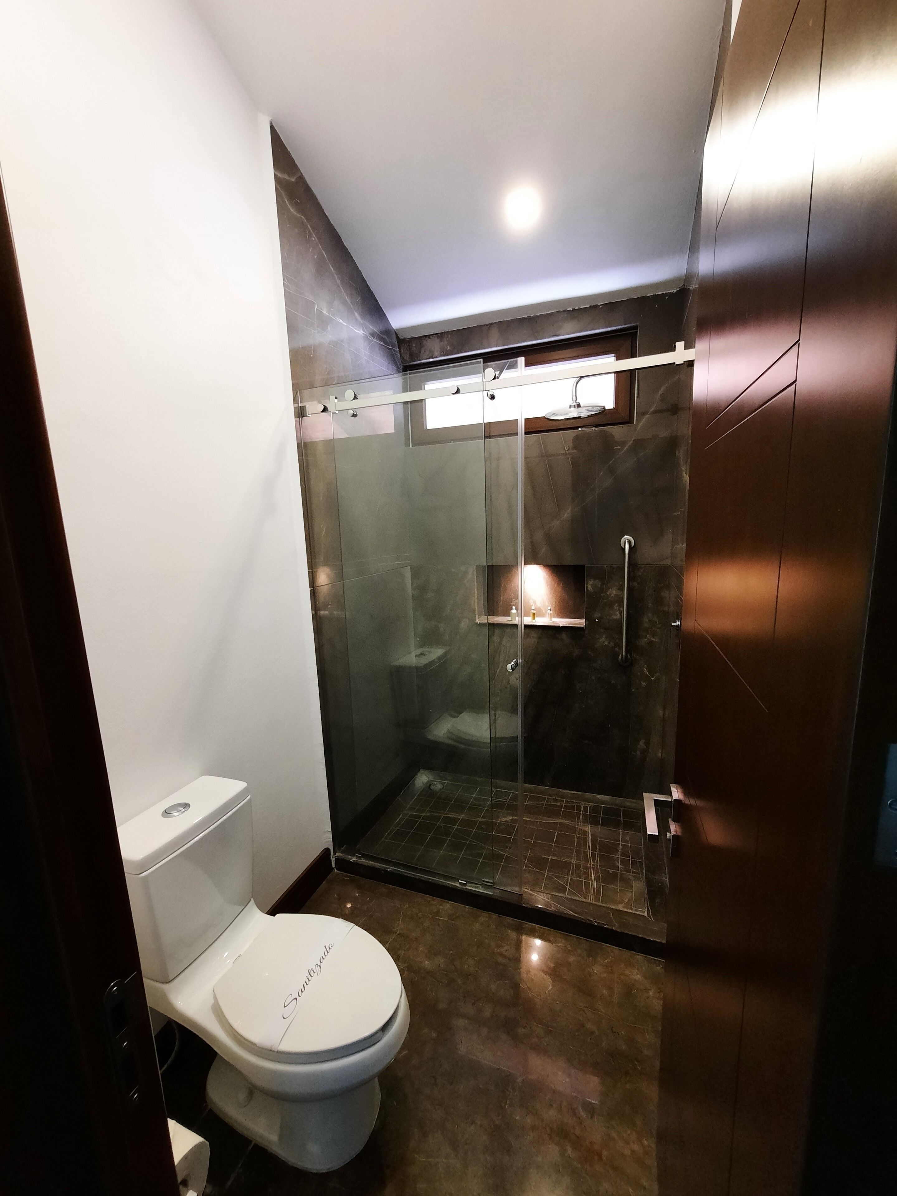 Uma casa de banho moderna com cabine de chuveiro em vidro, sanita branca e chão em mármore.