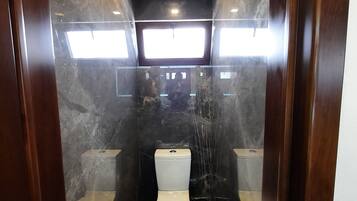Un baño moderno con inodoro blanco, piso de mármol y mampara de vidrio.
