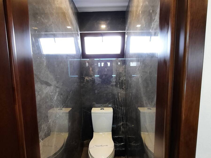 Un baño moderno con inodoro blanco, piso de mármol y mampara de vidrio.