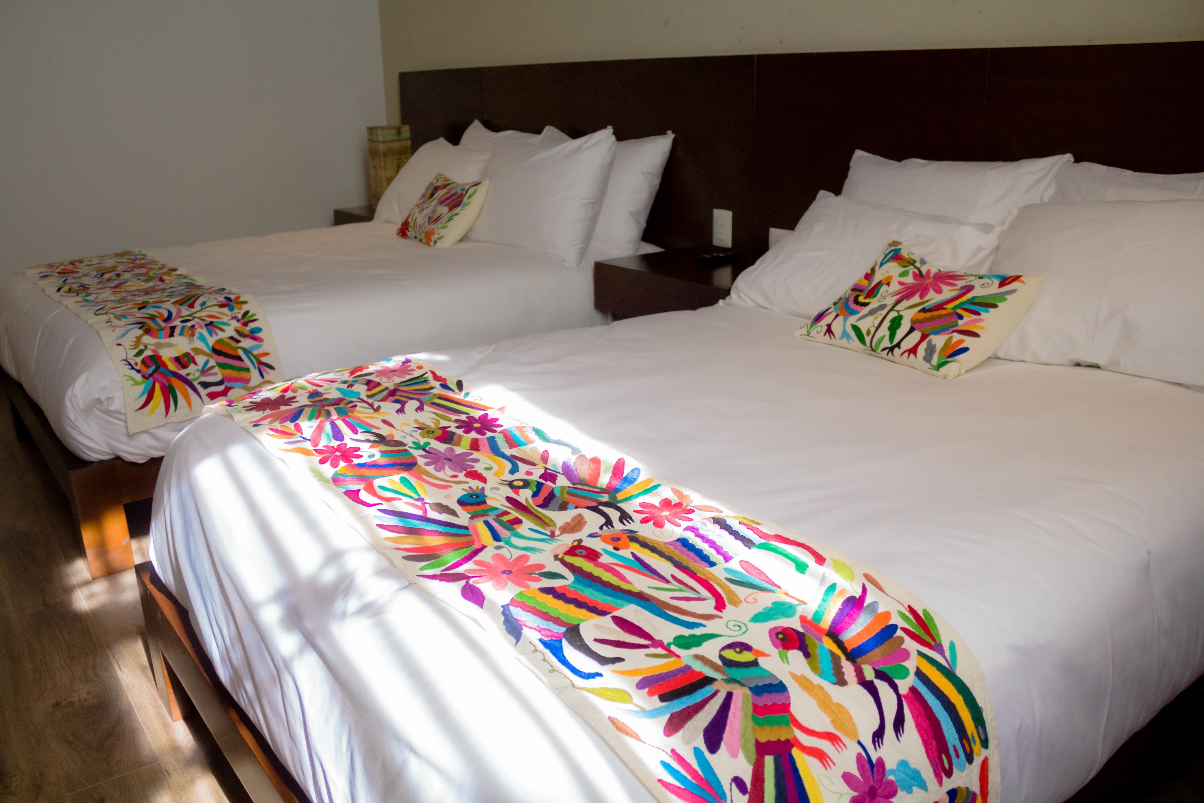 A hotel room with two single beds, each with a colorful floral bedspread and white pillows.