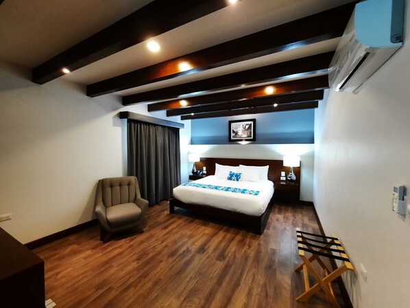 Habitación de hotel con una cama grande, una silla, una mesita de noche y un equipo de aire acondicionado.