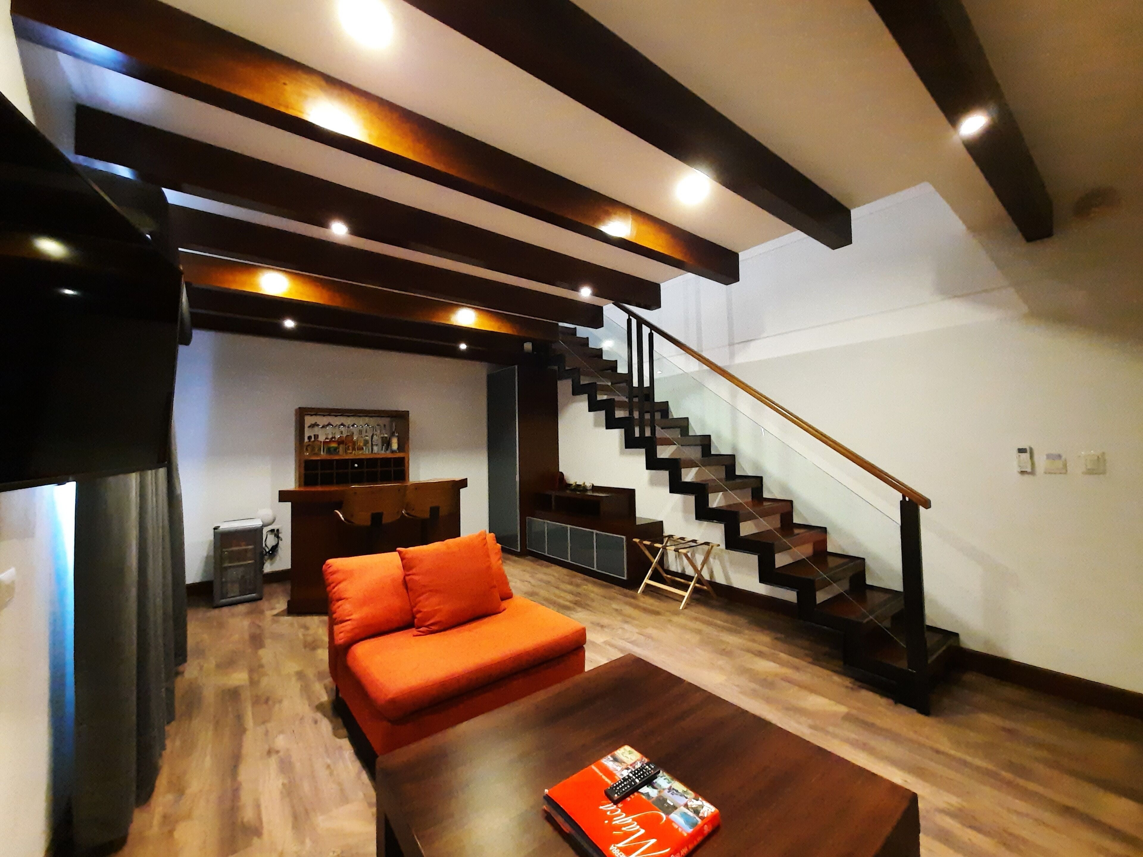 A modern living room with a sofa, a coffee table, a staircase, and a bar area.