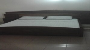 A bedroom with a wooden bed, a nightstand, and a wall-mounted light. - Nella Hotel (Agboville)