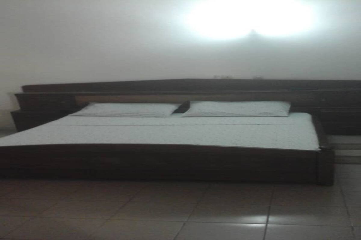 A bedroom with a wooden bed, a nightstand, and a wall-mounted light.