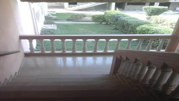 A staircase leading to a balcony with a view of a well-maintained lawn and bushes. - Nella Hotel (Agboville)
