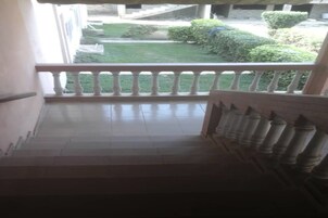 Una escalera lleva a un balcón con vistas a un césped cuidado y arbustos.