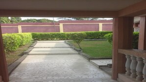 A covered walkway with a tiled floor leading to a grassy area. - Nella Hotel (Agboville)