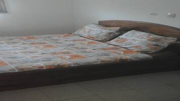 A single bed with a floral-patterned bedspread and matching pillows in a room with white walls and tiled flooring.