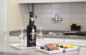 Un comptoir de cuisine avec une bouteille de porto Tawny de la marque Porto Cruz, deux verres à vin vides et un plateau contenant divers amuse-gueules.