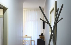 Un couloir avec un cadre de porte en bois, un luminaire fixé au mur et une fenêtre avec des stores.