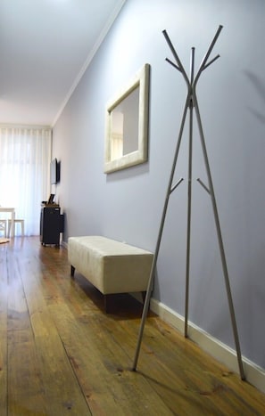 Une pièce avec un plancher en bois, un banc, un porte-manteau et un miroir au mur.