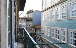 A narrow alleyway between buildings with a metal railing, a blue building with white window frames, and a grey building with a green awning. - Market Place I (Porto)