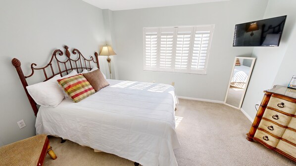 A bedroom with a bed, a dresser, a television, and a window with blinds.