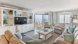 A living room with a TV, seating, and a balcony with a view.