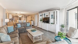 A spacious living room with a sectional sofa, a coffee table, and a TV mounted on a white cabinet.