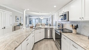 A modern kitchen with white cabinetry, granite countertops, stainless steel appliances, and a view to the living area.