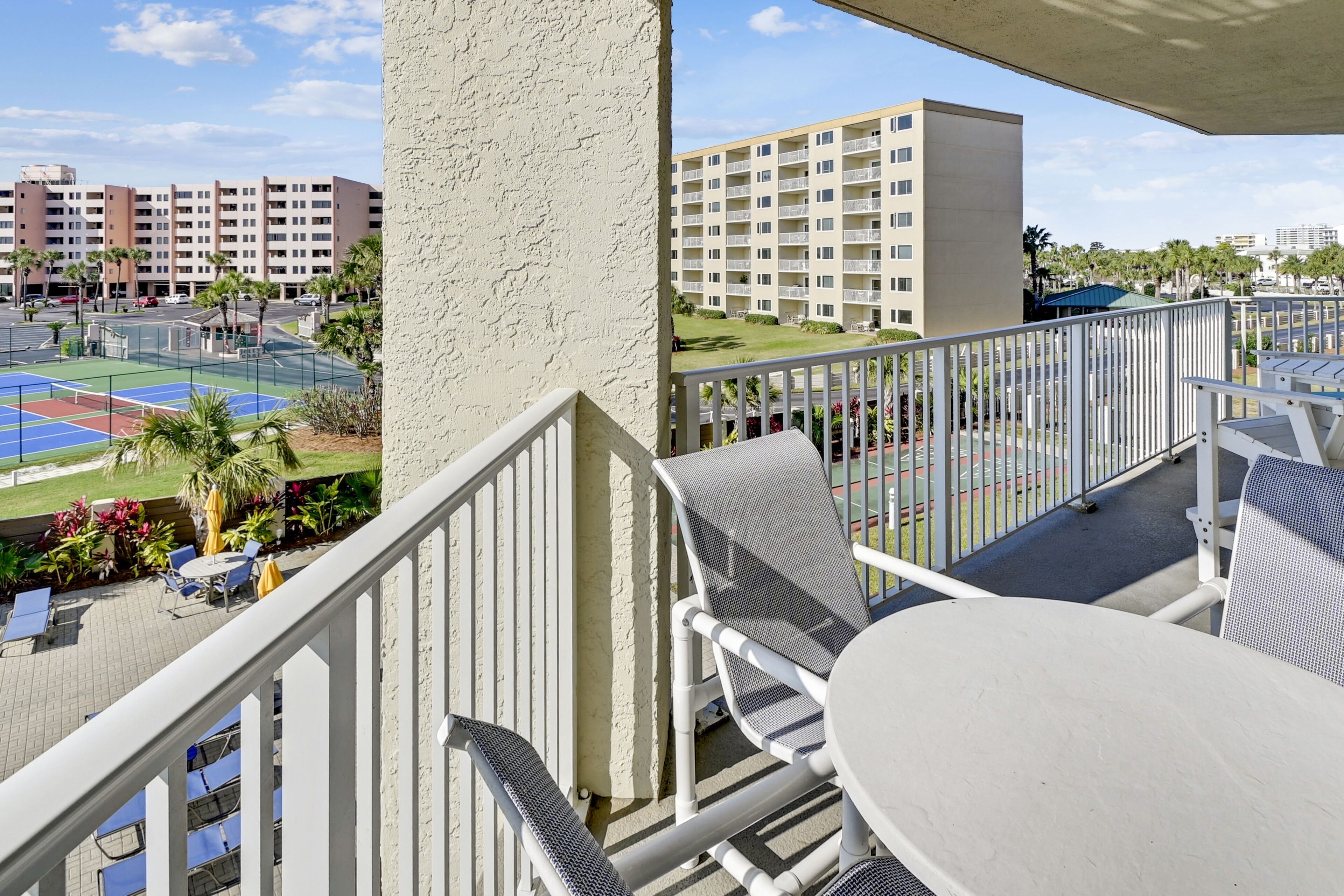 A balcony with outdoor seating, a tennis court, and a view of a multi-story building.