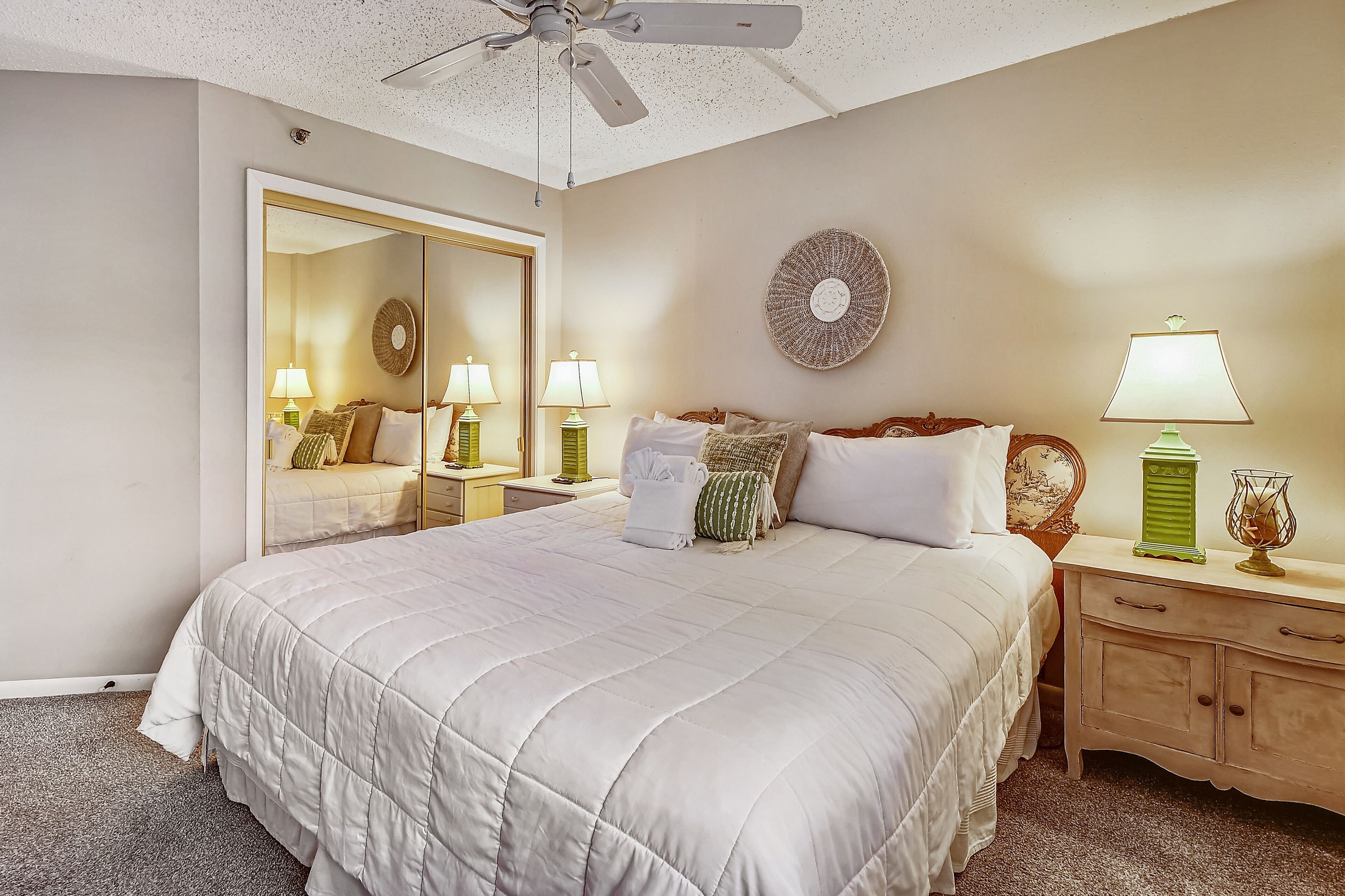 A neatly arranged bedroom with a large bed, bedside tables, a mirror, and a ceiling fan.