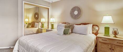 A neatly arranged bedroom with a large bed, bedside tables, a mirror, and a ceiling fan.